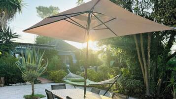 An outdoor patio with a table and chairs, a large umbrella, and a hammock.