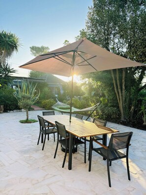 An outdoor patio with a table and chairs, a large umbrella, and a hammock.