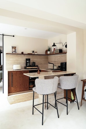 A modern kitchen with a central island, bar stools, and a coffee machine.