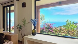 A room with a large window offering a view of the sea and colorful plants outside.