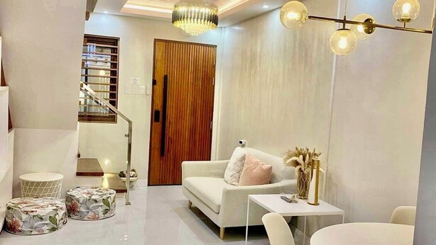 A modern living room with a white sofa, a dining table with chairs, and a chandelier. - Charming 2-BR House in San Jose Del Monte w/ WiFi, 3 split-type ACs, & Netflix (San Jose Del Monte)