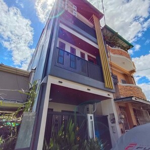 A multi-story building with balconies, a gated entrance, and a clear sky.