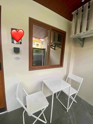 A small balcony with a white metal table and chair, a window with a brown frame, and a sign prohibiting smoking.