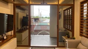A modern living room with a television, a sofa, and a sliding glass door leading to a balcony. - Charming 2-BR House in San Jose Del Monte w/ WiFi, 3 split-type ACs, & Netflix (San Jose Del Monte)
