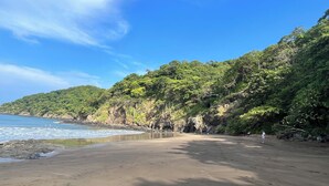 A beach with a clear sky, calm sea, and lush green hills in the background. - Relax in Costa Rica Pura Vida Style and enjoy the magic! (Coco)