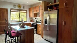 A kitchen with wooden cabinets, a stainless steel refrigerator, a built-in oven, and a window with a view of trees. - Relax in Costa Rica Pura Vida Style and enjoy the magic! (Coco)