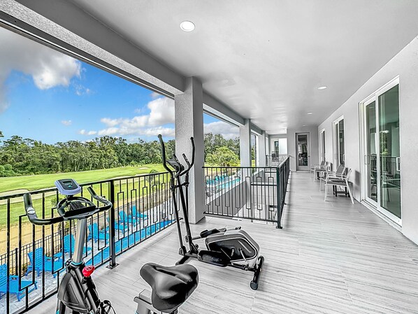 A balcony with exercise equipment, a pool, and a view of a golf course.