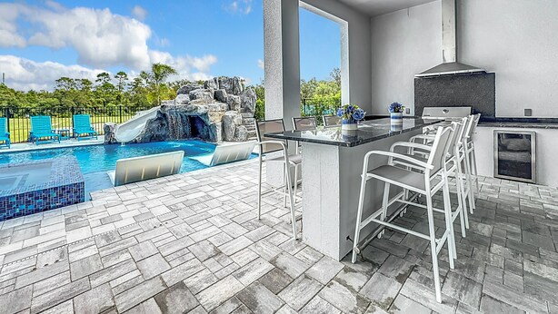 A poolside area with a waterfall, bar seating, and a grill. - Really Fun House with tons of room, huge pool plenty to do and a terrific view  (Kissimmee)