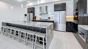A modern kitchen with a large island, bar stools, stainless steel appliances, and a sleek design. - Really Fun House with tons of room, huge pool plenty to do and a terrific view  (Kissimmee)