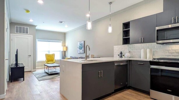 Una cocina moderna con armarios oscuros, horno de acero inoxidable y luces colgantes.