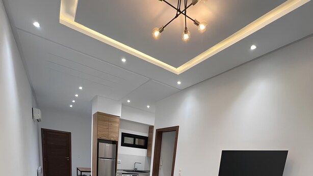 Un salon moderne avec un canapé, un pouf et un téléviseur à écran plat fixé au mur.