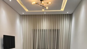 Un salon moderne avec un canapé d’angle, une petite table basse, un téléviseur fixé au mur et un luminaire suspendu au plafond.