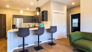 A modern kitchen with a central island, three bar stools, and a green sofa. - 223  Brand New 2 Bdrm, 2 BATH, 1 Liv, 1 Kith (Dunellen)