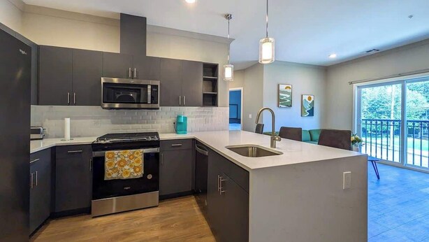 A modern kitchen with dark cabinetry, stainless steel appliances, and a large island with a sink. - 223  Brand New 2 Bdrm, 2 BATH, 1 Liv, 1 Kith (Dunellen)