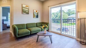 A living room with a green sofa, a round coffee table with flowers, and a large sliding glass door to the outside. - 223  Brand New 2 Bdrm, 2 BATH, 1 Liv, 1 Kith (Dunellen)
