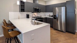 Une cuisine moderne dotée d’un îlot central, d’appareils électroménagers en acier inoxydable et de tabourets de bar.