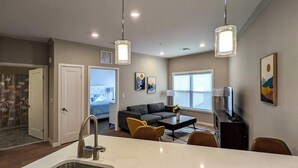 A modern kitchen with a large island, a dining area with yellow chairs, and a living room with a sofa and artwork. - 210 Brand New 1 Bedroom, 1 Bath, 1 Full Kit, 1 Liv (Dunellen)