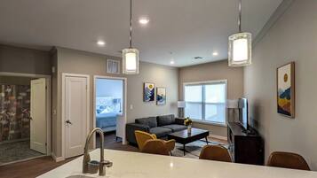 A modern kitchen with a central island, dining area with chairs, a sofa, and artwork on the walls.