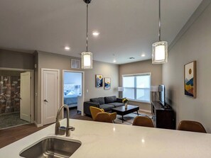 A modern kitchen with a central island, dining area with chairs, a sofa, and artwork on the walls.