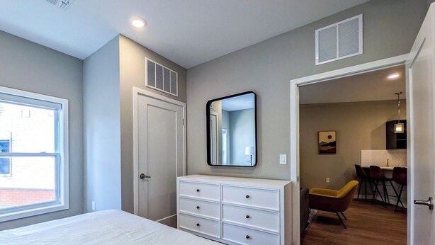 Une chambre à coucher comprenant un lit, une commode, un miroir, une fenêtre et une porte donnant sur un coin repas.