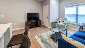 Una sala de estar moderna con televisor de pantalla plana, un sofá azul, un sillón estampado y una mesa de centro de vidrio.