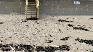 Une propriété située en bord de mer, dotée d’un escalier en bois menant à une plage privée, d’une grande maison avec de nombreuses fenêtres et d’un panneau indiquant « PLAGE PRIVÉE ».