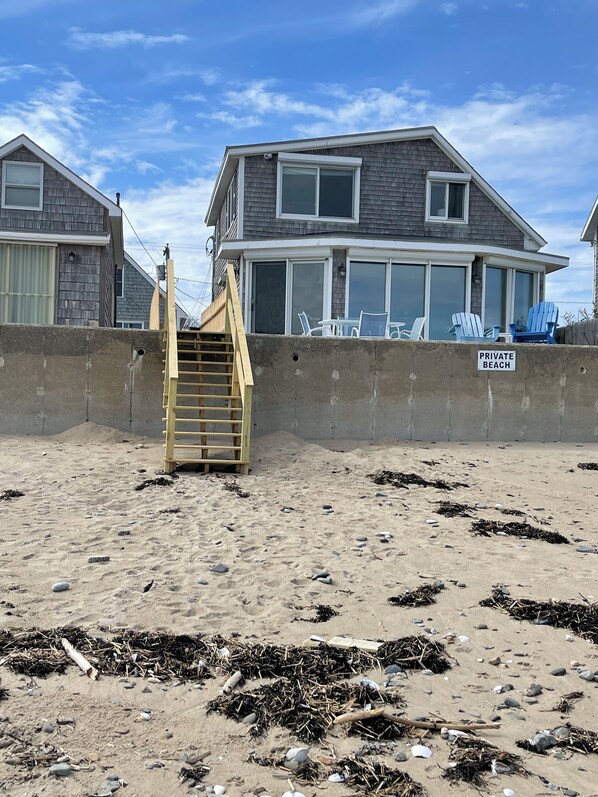 Une propriété située en bord de mer, dotée d’un escalier en bois menant à une plage privée, d’une grande maison avec de nombreuses fenêtres et d’un panneau indiquant « PLAGE PRIVÉE ».