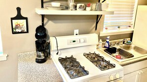 Una cocina con estufa a gas, cafetera y repisas que sostienen platos y vasos.