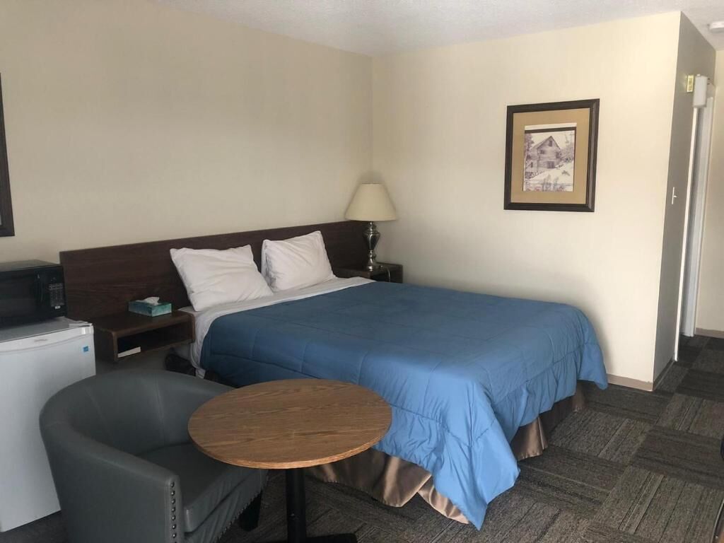 Ein Hotelzimmer mit Bett, Schreibtisch, Stuhl, Lampe und einem Bild an der Wand.