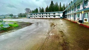 A motel with a row of rooms, a parking lot, and a forested background. - Houston Motor Inn (Houston)