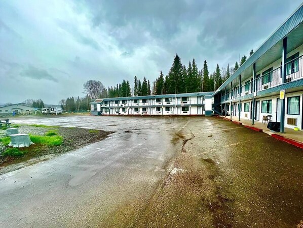 A motel with a row of rooms, a parking lot, and a forested background.