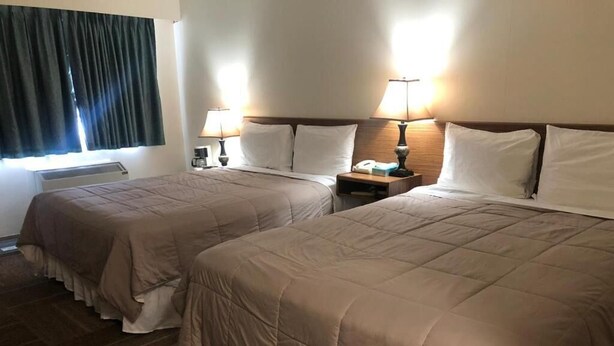A hotel room with two beds, each with a headboard, bedside tables with lamps, and a window with curtains. - Houston Motor Inn (Houston)