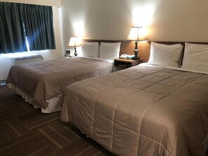 Habitación de hotel con dos camas, cada una con cabecero, mesitas de noche con lámparas y una ventana con cortinas.