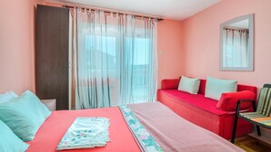 Une chambre à coucher avec un lit, un canapé rouge, une chaise, une grande fenêtre avec des rideaux légers et un miroir au mur.