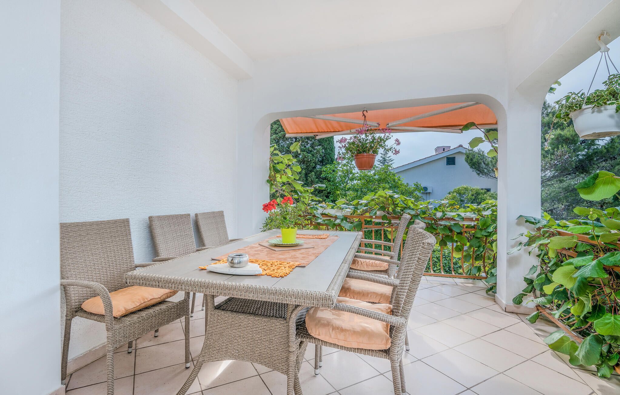 Eine Terrasse im Freien mit Tisch und Stühlen, umgeben von Blumentöpfen und Blick auf einen Garten.
