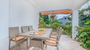 Une terrasse extérieure avec une table et des chaises, entourée de plantes en pot et offrant une vue sur un jardin.
