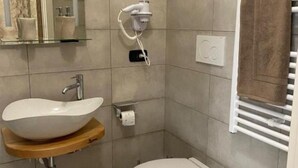 Een badkamer met een witte wastafel, toilet, handdoekhouder en een haardroger bevestigd aan de muur.