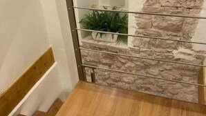 Een trap met houten treden en een metalen leuning, die leidt naar een stenen muur met een plant op de bovenste plank.