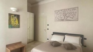 Een slaapkamer met een bed, een bankje, een deur en een schilderij aan de muur.