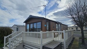 A mobile home with a deck, a small outdoor area, and a tree. - Mini Lodge Robin Hood Holiday Park (Rhyl)