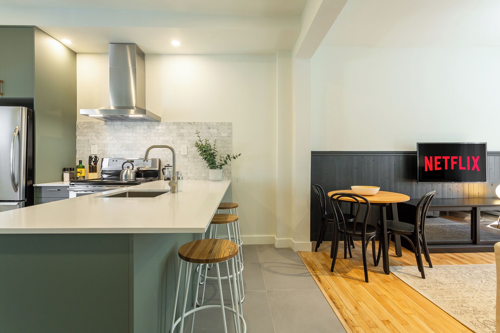 A modern kitchen with a large island, a dining area with a table and chairs, and a TV displaying the Netflix logo.