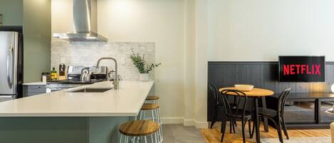 A modern kitchen with a large island, a dining area with a table and chairs, and a TV displaying the Netflix logo.
