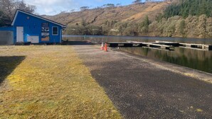 A blue building with a sign for "Activity Days" near a calm lake with docks. - Cozy Highland Retreat With Stunning Views (Invergarry)
