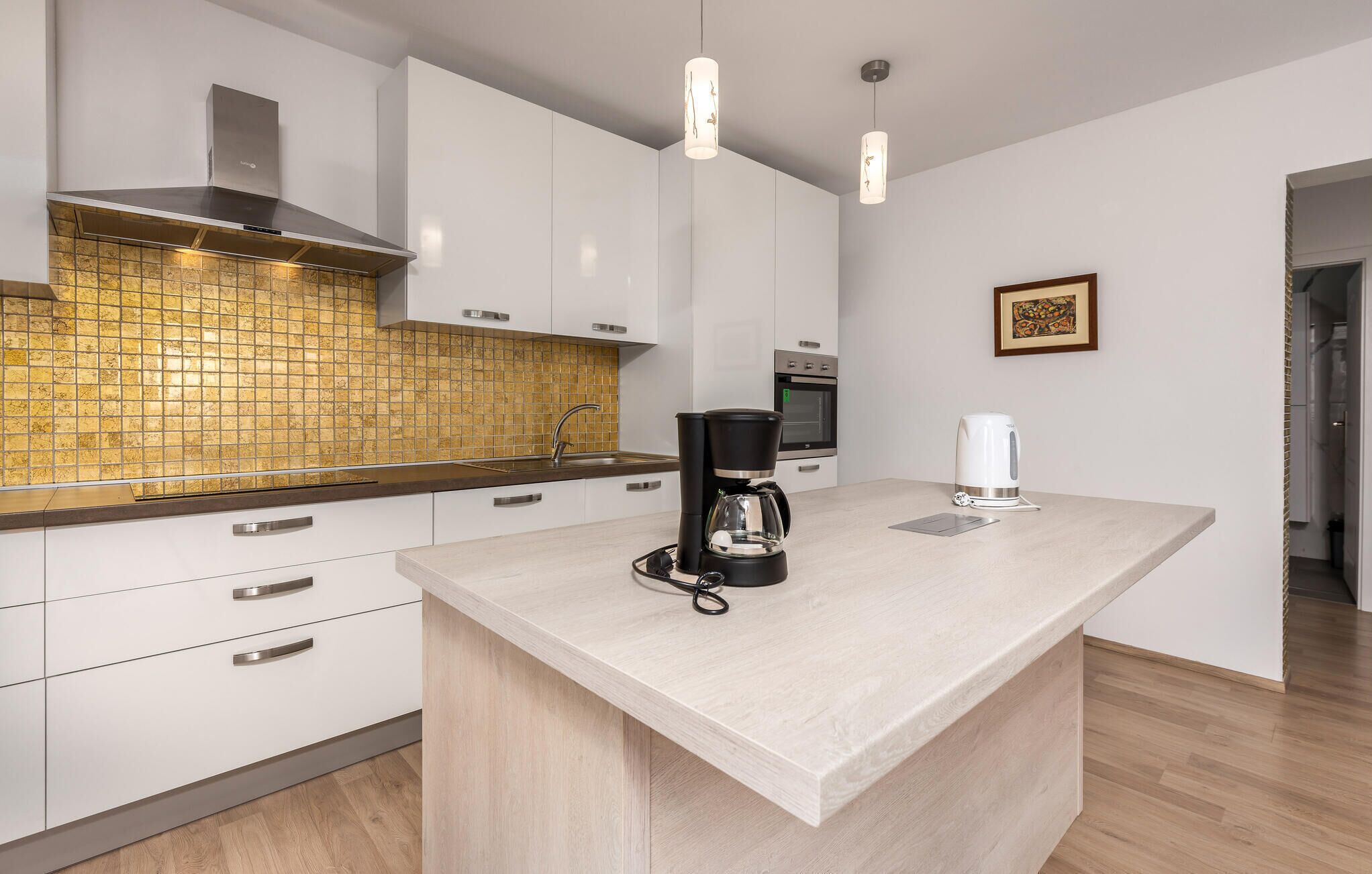 A modern kitchen with white cabinets, a wooden backsplash, a coffee maker, and a kettle on the counter.