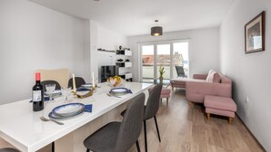 Una sala de estar moderna con un sofá blanco, un sofá rosa y una zona de comedor con una mesa y sillas blancas.