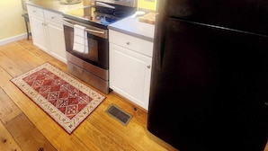 A compact kitchen with white cabinets, a stainless steel stove, and a black refrigerator. - Cozy Loblolly Loft in charming Summerville (Summerville)