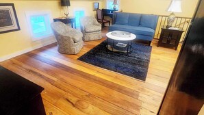 A loft-style living room with a high ceiling, wooden flooring, a blue sofa, patterned armchairs, a coffee table, and a piano. - Cozy Loblolly Loft in charming Summerville (Summerville)