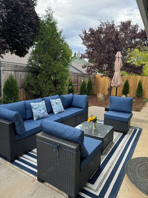 A patio area with a blue sofa set, a small table with a vase of flowers, and a striped rug. - Beautiful & Comfortable Home in Central Point (Central Point)