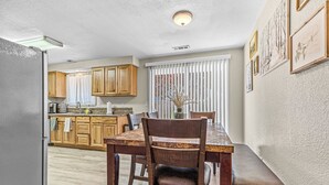 A kitchen with wooden cabinets, a dining table with chairs, and a window with blinds. - Beautiful & Comfortable Home in Central Point (Central Point)