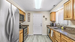 A kitchen with wooden cabinets, stainless steel appliances, a microwave, and a door with a coffee-themed decoration. - Beautiful & Comfortable Home in Central Point (Central Point)